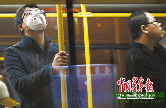 10月25日，北京某公交车内，一位男青年戴着口罩抬头张望。连日来，包括京津冀在内的华北等地遭遇雾霾天气。本报记者 陈剑 摄